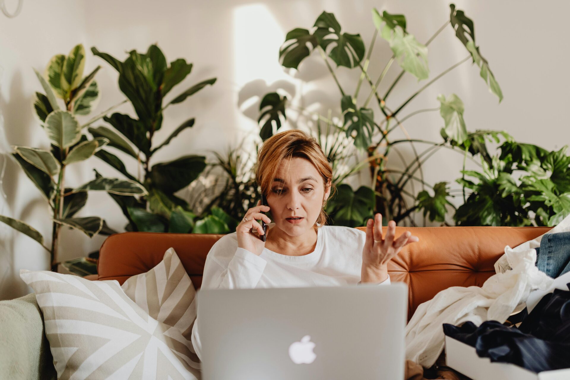 ambiente de sala com mulher trabalhando em laptop e ao fundo diversas plantas de flohagem grande.