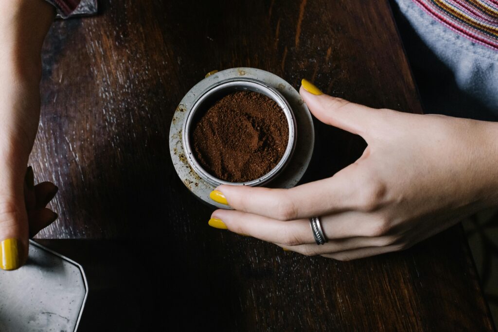 Mãos segurando um recipiente com borra de café fresca, pronta para ser reutilizada como adubo natural em orquídeas.